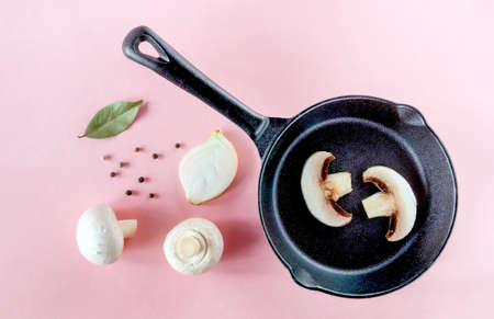 Small black cast iron skillet with champignon slices, mushrooms, onions and spices on a pink surface. Horizontal orientation, selective focus, top view.の写真素材
