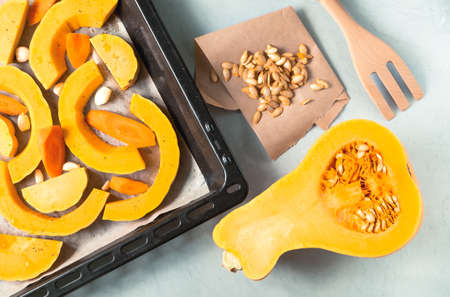 Half ripe pumpkin with seeds, pumpkin and carrot slices on a baking sheet. Healthy food concept. Horizontal orientation, selective focus, top view.の写真素材