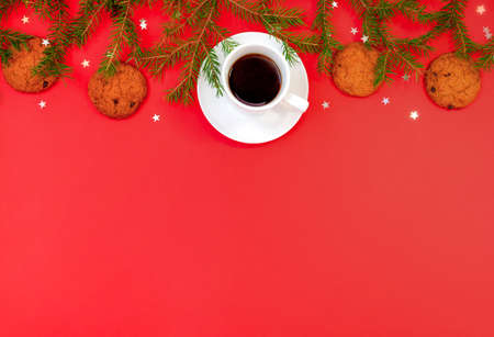 Christmas background with fir branches, a cup of coffee and oatmeal chocolate chip cookies on a bright red background with copy space. Horizontal orientation, selective focus.の写真素材