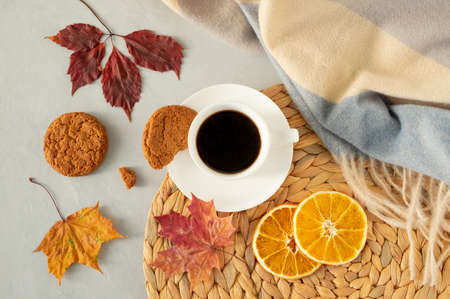 Flat lay from a cup of black coffee on a gray background with autumn leaves, a warm cape, a wicker napkin, oatmeal cookies and slices of dried oranges. Horizontal orientation, selective focus.の写真素材