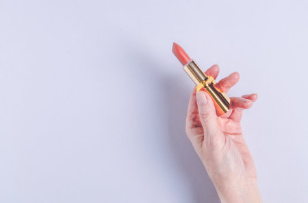 A female hand holds an open case with bright pink lipstick on a lilac background. Decorative cosmetics concept. Selective focus, horizontal orientation.の写真素材