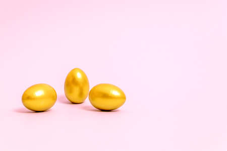 Three Easter eggs decorated with gold paint on a pink background. Concept for Easter, spring. Selective focus. Copy space.の写真素材