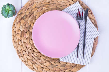 Close-up top view of a serving of empty pink plates, a knife and a fork on a straw eco-friendly napkin. Selective focus. Mockup, minimalism.の写真素材