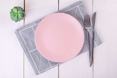 Close up top view of serving empty pink plate, knife and fork on folded linen napkin with geometric...