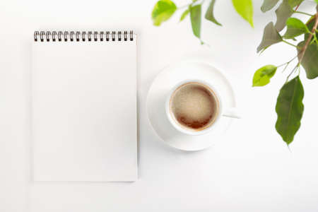 Mockup top view of an open blank notebook on a spiral,, white porcelain cup with coffee and leaves...