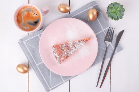 A piece of pie on a pink plate with a knife and fork on a folded linen napkin with a geometric pattern and a mug of coffee. Golden Easter eggs. Homemade baking. Selective focus.View from above.の写真素材