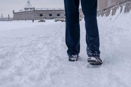 Legs of a walking man in trousers and winter boots in deep snow against the backdrop of a snowy landscape. Selective focus.の写真素材