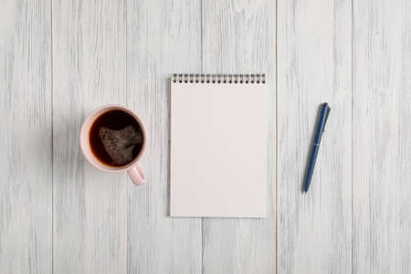 Top view of a mockup of a blank notepad, a cup of coffee and an automatic ballpoint pen on a light painted wooden surface. Selective focus. Copy space.の写真素材