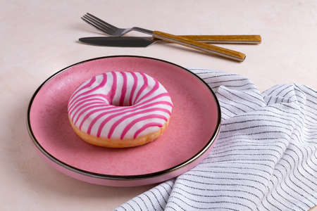 Sugar-coated donuts lie on a pink ceramic plate. Serving with cutlery and linen napkin. Selective focus.の写真素材