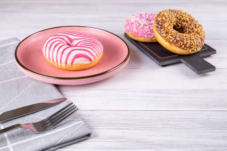 Three sugar-coated donuts lie on a pink ceramic plate and a slate board. Serving with cutlery and linen napkin. Selective focus. Copy space.の写真素材
