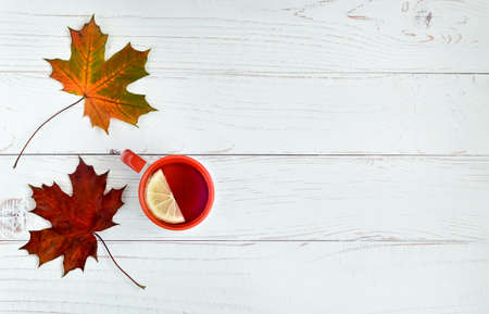 Light wooden background with autumn leaves of girlish grapes, ivy and a cup of tea with lemon. Autumn season. Horizontal orientation, selective focus.の写真素材