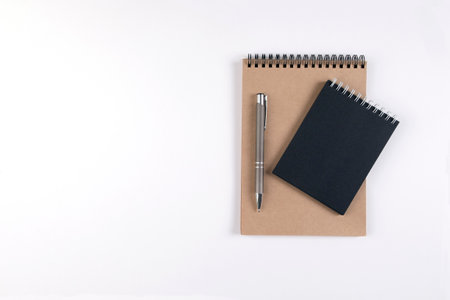 Two blank spiral notepads stacked on a white background next to an automatic pen. Notepads with...