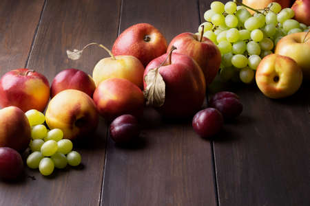 Ripe fresh autumn fruits apples, nectarines, plums and grapes lie on dark wooden surface. Harvest, healthy and vegetarian food.の写真素材