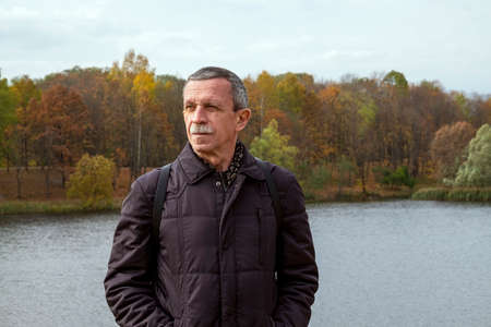 Adult retired man stands by the lake on beautiful autumn day and is resting. Slowdown concept. Selective focus.の写真素材