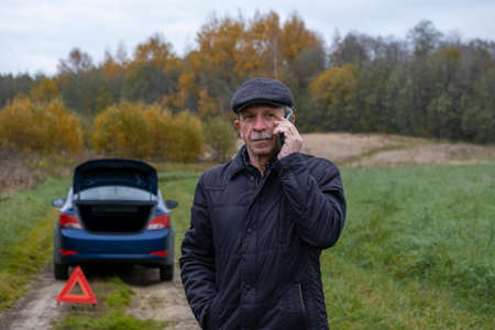 Adult pensioner calls technical assistance on smartphone after his faulty car outside city. Selective focus.の写真素材