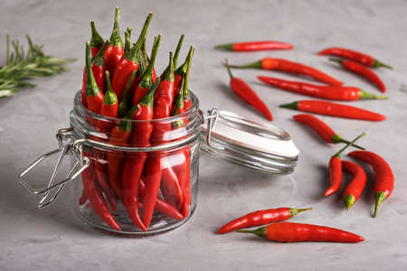 Bright red hot pepper in glass jar and scattered on gray surface with a plaster texture. Selective focus.の写真素材