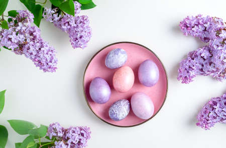 Close-up top view of beautiful nacreous pink and lilac easter eggs lie on a pink plate framed by...