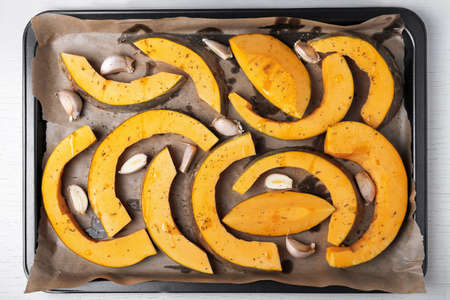 Large pieces of pumpkin are laid out on parchment paper on baking sheet with olive oil, garlic and dry herbs. Healthy and vegetarian food. Selective focus, top view.の写真素材