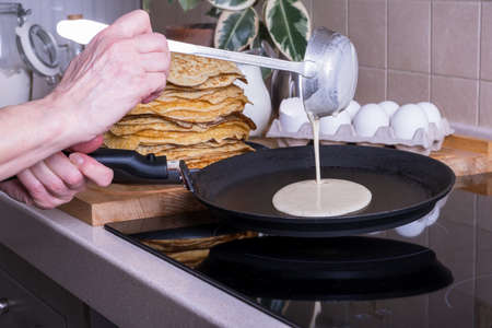 Housewife woman bakes pancakes for breakfast and pours dough into hot frying pan. Homemade...