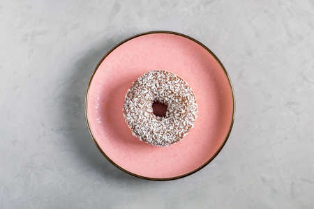 Donut with coconut topping lies on a pink ceramic plate on a gray background. View from above. Selective focus.の写真素材