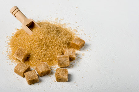 Brown cane sugar is also sprinkled in lumps on a light surface. Wooden scoop for bulk products. Selective focus. Space for text.の写真素材