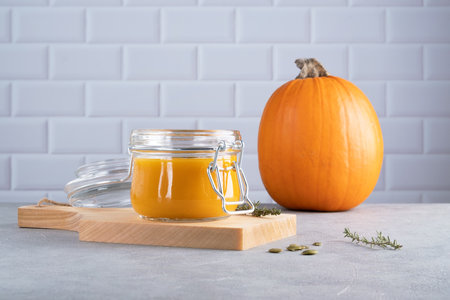 Pumpkin puree soup with pumpkin seeds and thyme in a glass jar on a wooden kitchen board. Ripe pumpkin. Healthy diet. Selective focus.の写真素材