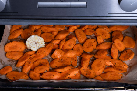 Fresh raw carrots cut into pieces with spices on a baking tray in the oven. Selective focus.の写真素材