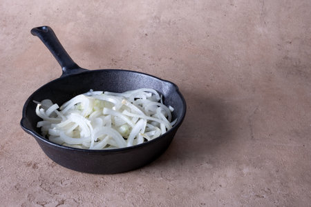 Close-up of a frying pan with chopped onions standing on a dark surface. Selective focus.の写真素材