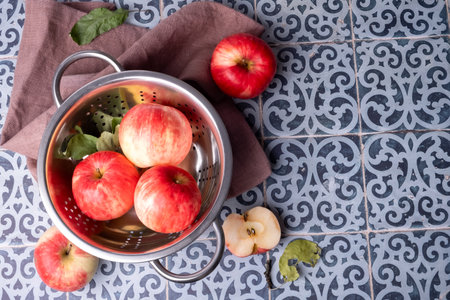 Ripe red apples lie on a linen napkin and in a colander on a table with a blue-green tile surface. Selective focus.の写真素材