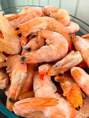 A close-up image of frozen shrimp piled in a bowl. The shrimp are covered in frost, highlighting their freshness and suitability for various seafood recipes and culinary creations.の写真素材