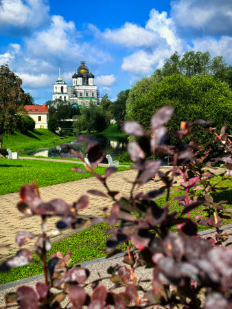 Pskov, Pskov Oblast, Russia - August 9, 2025. Scenic view of the Holy Trinity Cathedral with lush greenery and a riverbank in the foreground.のeditorial素材