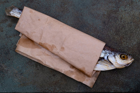 Salted dried sabrefish wrapped in brown paper on a gray surface demonstrates traditional seafood preservation packaging. Selective focus.の写真素材