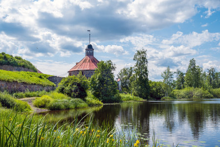 Priozersk, Leningrad Oblast, Russia - 06.28.2025. Korela Fortress stands by a serene river, surrounded by lush greenery and blooming flowers. .のeditorial素材