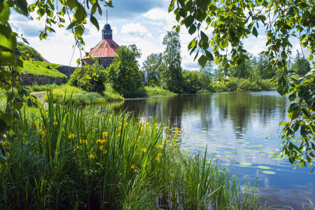 Priozersk, Leningrad Oblast, Russia - 06.28.2025. Korela Fortress stands by a serene river, surrounded by lush greenery and blooming flowers. .のeditorial素材