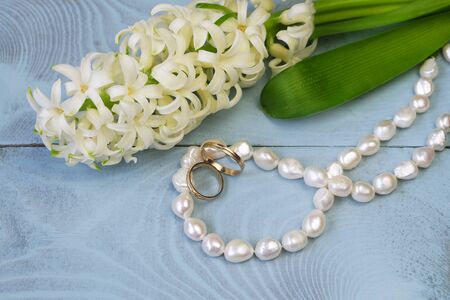 White hyacinth, pearl beads and wedding rings on a blue background, composition with jewelry, greeting card, invitation to the wedding day.の写真素材