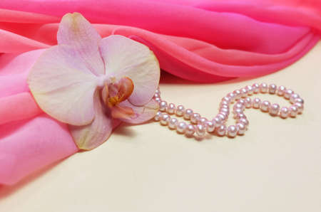 Peach phalaenopsis flower on pink chiffon drapery with pearl beads, composition with flower and jewelry, selective focus, horizontal orientationの写真素材