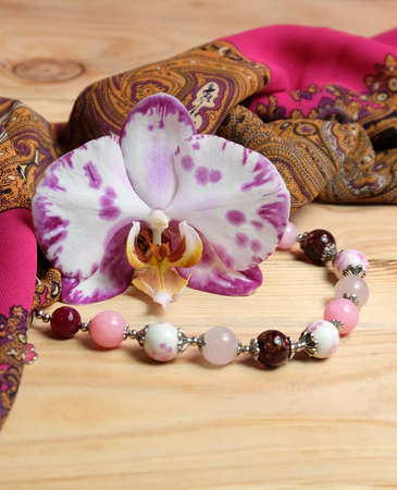 Composition with orchid flower, silk scarf and bracelet made of porcelain beads and stones for greeting card, magazine cover, etc., vertical orientation, selective focus.の写真素材