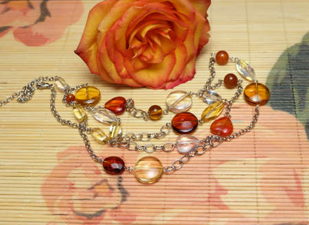 Orange rose and glass beads on a chain on a bamboo napkin, composition with handmade womens jewelry for birthday, mother's day, Valentine's day and other holidays, selective focus.の写真素材
