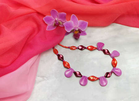 Czech glass beads with orchid flowers on a background of pink chiffon drapery, composition with handmade women's jewelry, with space for an inscription, selective focus, horizontalの写真素材