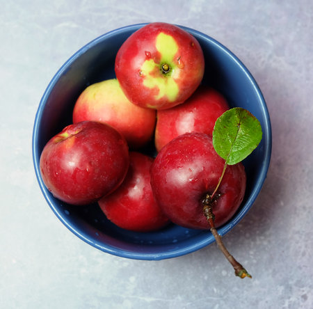 Red-yellow apples in a blue ceramic bowl on a light background, top view, selective focus, square format.の写真素材