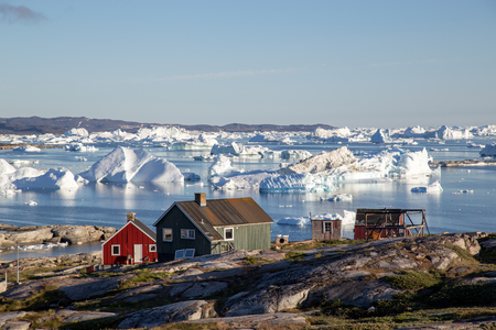 Rodebay, Greenland - July 09, 2018: Colorful wooden houses with icebergs in the background. Rodebay, also known as Oqaatsut is a fishing settlement north of Ilulissat.のeditorial素材