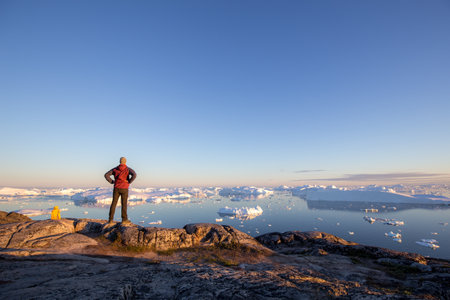Young man looking at the Ilulissat Icefjord during midnight sun.の写真素材