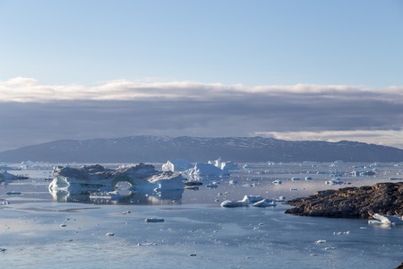 Ilulissat, Greenland - July 9, 2018: The coastline and icebergs during midnight sun. Rodebay, also...