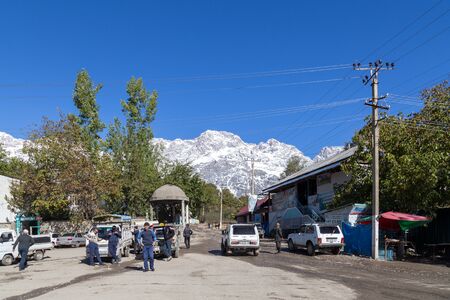 Arslanbob, Kyrgyzstan - October 10, 2014: People and cars on the townsquare with snowy mountains in...