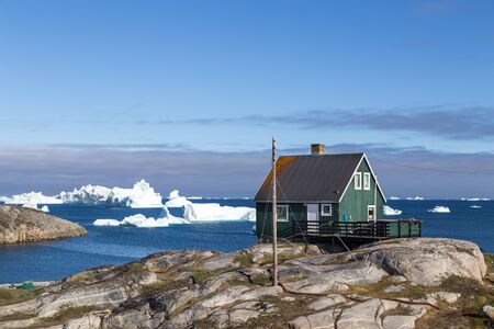 Qeqertarsuaq, Greenland - July 05, 2018: A green wooden house with icebergs in the backgroundのeditorial素材