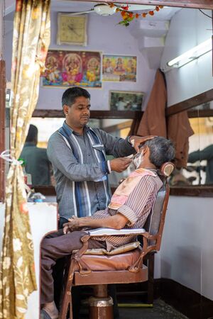 Jaisalmer, India - December 6, 2019: A barber shaving a customer in his barber shop.のeditorial素材