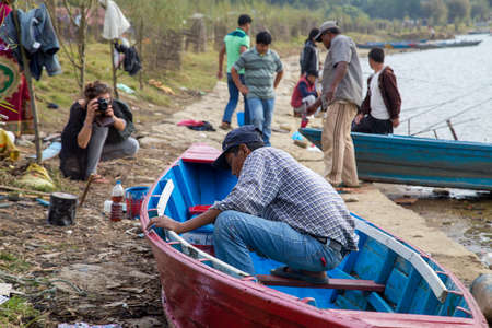Pokhara, Nepal - November 16, 2014: A Nepalese man repairing a wooden boat at the shores of Phewa Lake.のeditorial素材