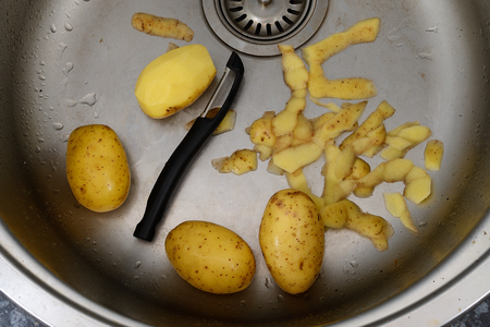 vegetable peeler, potatoes and potato peelings in the kitchen sinkの写真素材