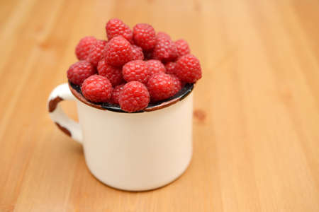 large ripe raspberries in a mug on a wooden background