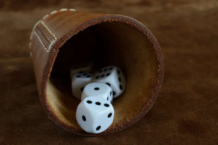 dice and leather cup on a leather surface, devils bones represent randomness and luck, old gambling